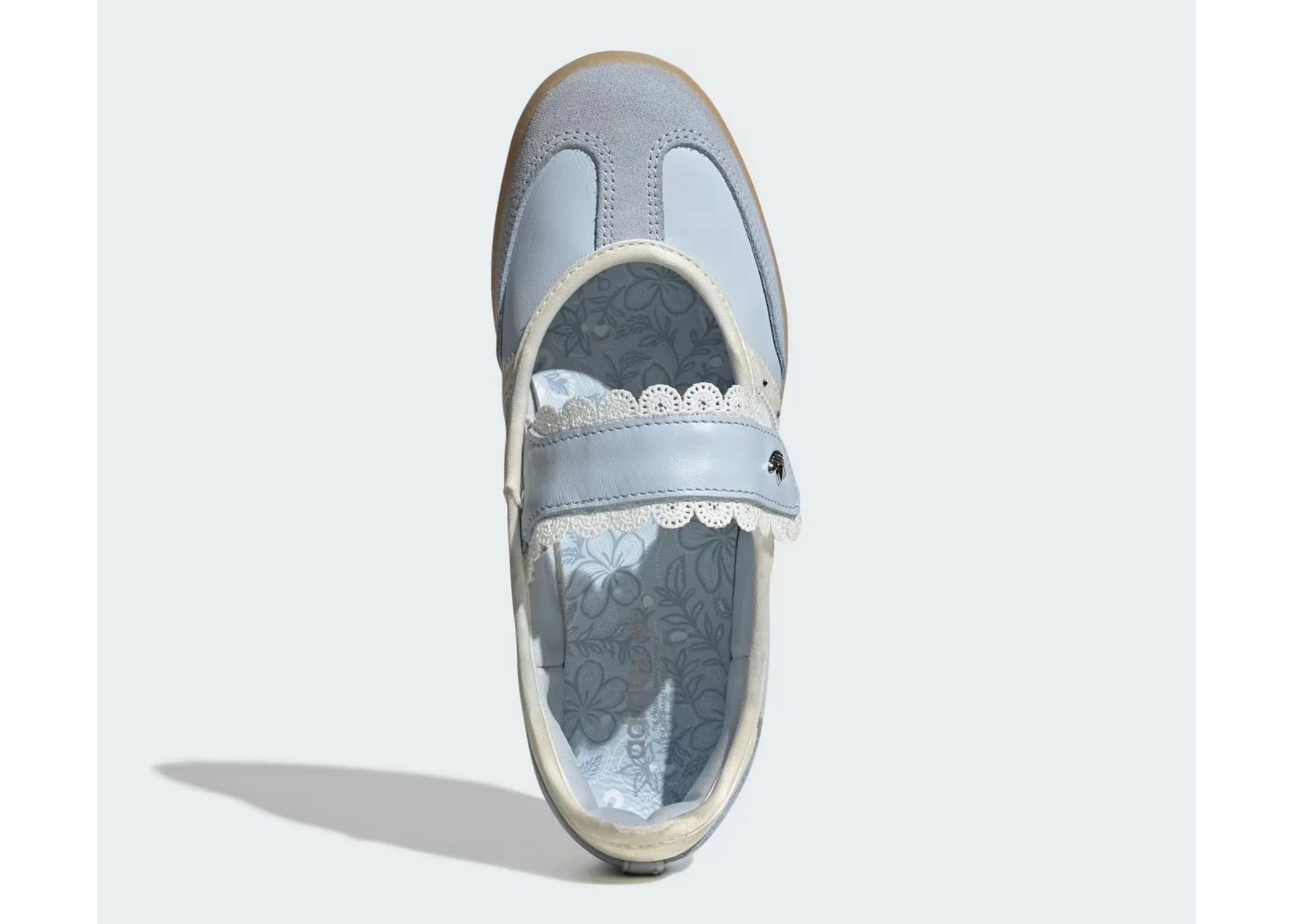 A single light blue Mary Jane style shoe shown from a top-down view on a light gray background. The shoe features a light blue leather strap with white lace trim, a light blue suede upper, and a patterned lining.