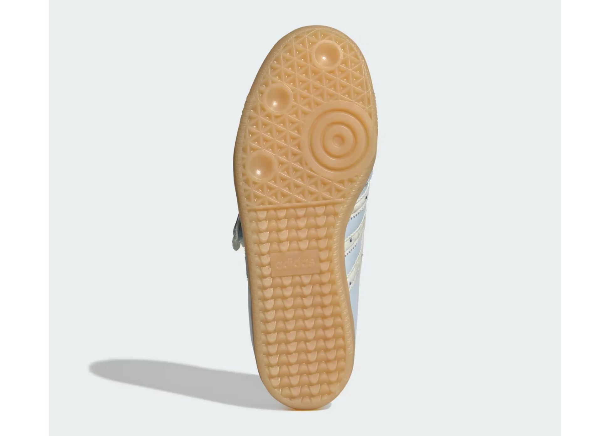 The outsole of a light blue and white sneaker, showing a textured tan rubber tread with circular grip patterns, photographed against a light gray background.